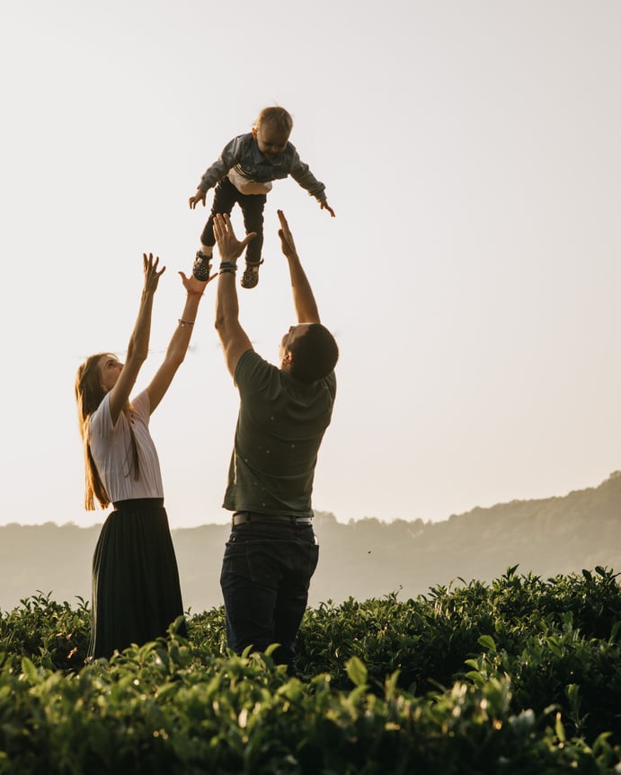 a female and a male holding a child in the air while standing in a field