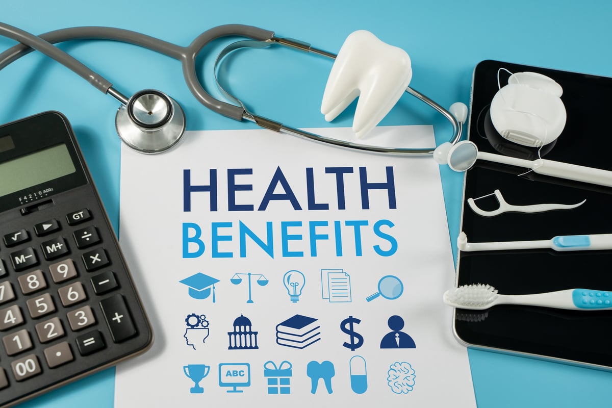 health benefits on a paper with a calculator, stethoscope, toothbrush, and other health related items on a blue background