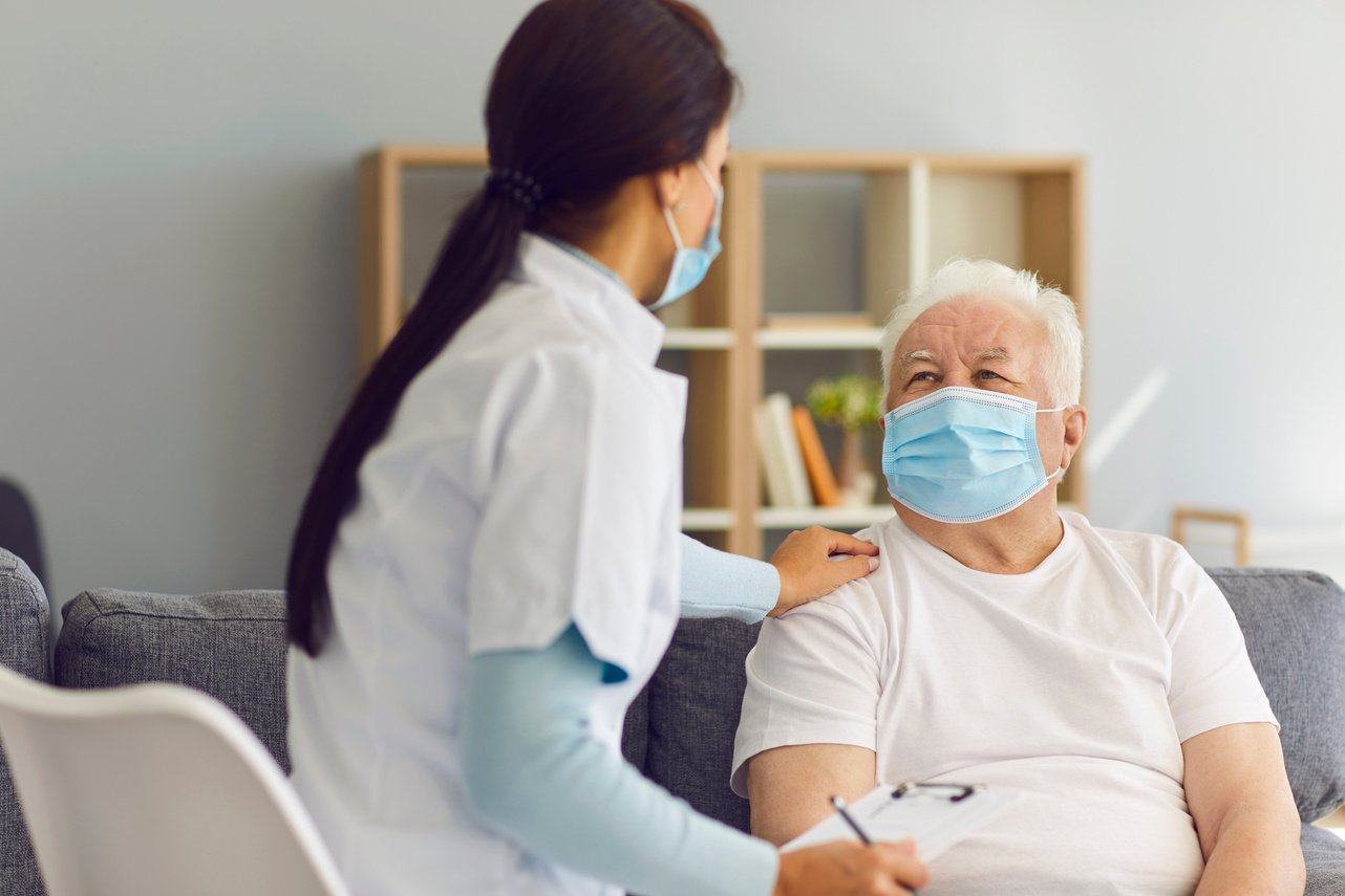 an individual sitting on a couch with a nurse wearing a face mask